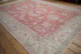 Distressed pale raspberry red Oushak field with floral blossoms and an ivory arabesque border.