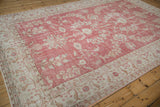 Corner of distressed Oushak rug with faded raspberry red field and ivory arabesque border.