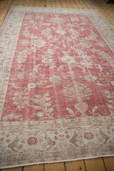 Faded ivory floral vines on distressed cochineal Oushak with arabesque border detail.