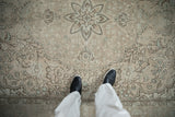 Feet on distressed Turkish Tabriz carpet, showing worn pile and faded floral patterns.