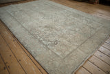 Distressed vintage Turkish Tabriz rug corner, displaying worn ivory floral motifs and serrated leaf border.