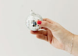 A small, round disco ball with reflective square mirror tiles held in a hand.