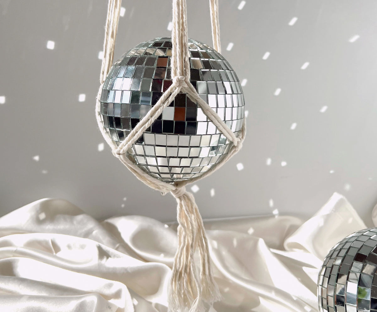 A mirrored disco ball held within a handmade, cream-colored macrame hanger.