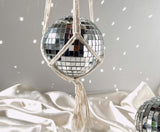 A mirrored disco ball held within a handmade, cream-colored macrame hanger.
