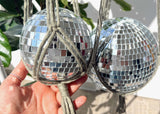 A hand holding a small, mirrored disco ball inside a knotted macrame hanger.