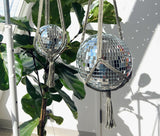 Two disco balls in macrame hangers reflecting spots of sunlight on a nearby wall.
