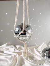 Disco ball in a cream macrame hanger casting reflections on a wall and silky fabric.