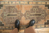 Turkish Kars runner rug, stepped medallions, scrolled motifs in muted tones, shown with boots for scale.
