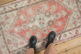 Feet on a distressed Oushak runner, revealing its pale red, seafoam, and ivory worn texture.