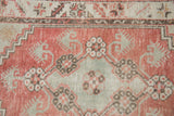 Close-up of a distressed Oushak runner with pale red, seafoam green, ivory finned blossoms and worn texture.