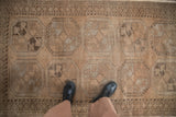 Close-up of vintage distressed Ersari rug, floral guls, varied texture in muted browns, with boots.