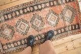 A person's view looking down at a vintage distressed Oushak runner on a wood floor.
