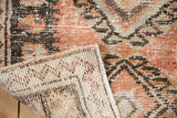 Folded corner of a distressed Oushak rug reveals its hand-knotted back and worn, textured pile.