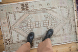 Distressed Oushak rug: worn ivory, brown, mauve pile showing hexagonal medallion and serpent motifs, with boots.