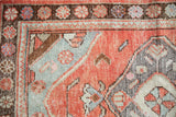 Distressed Oushak rug close-up, highlighting brick red orange and seafoam green floral patterns with textured wear.