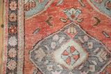 Distressed Oushak rug close-up: brick red orange field with central pinwheel blossom and wear.