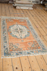 Distressed vintage Oushak rug with rust field, blue serpent border, and ivory floral detail.