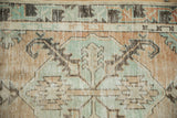 Distressed Oushak rug with shield medallion, seafoam green, beige, and terracotta, showing knot heads.