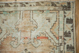 Distressed Oushak rug corner with time-softened beige, jade, terracotta hues and worn geometric pattern.