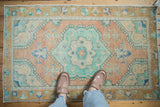 Distressed vintage Oushak rug featuring muted mint green and peach medallion, feet visible.