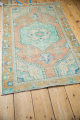 Distressed Oushak rug corner with shaded gold border, germinating plants, and foundation wear.