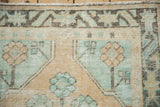 Distressed Oushak rug runner with mint green and dusty gold blossoms, geometric border, even pile wear.
