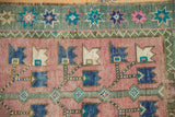 Distressed Oushak rug close-up: dusty blush serrated blossoms, starburst border.