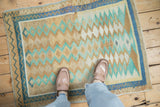 A vintage Oushak rug's distressed texture and boho diamond pattern in sand, mint, and denim blue.