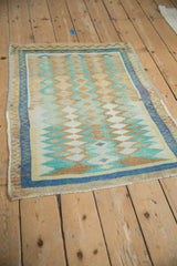 Angled view of a distressed Oushak rug with geometric diamond columns in sand, blue, and mint.