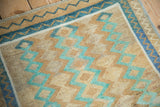 Corner detail of the distressed Oushak's texture and zig-zag border in sand, blue, and mint green.