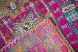 Folded Vintage Kars rug: vibrant magenta, teal, and gold geometric pile over its woven reverse.