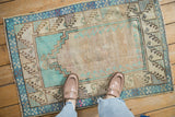 A vintage distressed Oushak rug styled on a floor, showing its scale and geometric turquoise patterns.