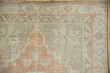 Vintage distressed Oushak rug corner with dusty blush and seafoam green pattern, showing pile wear.