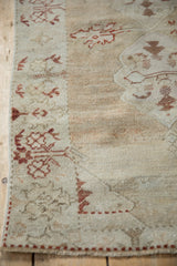 Close-up on the border of a distressed Oushak rug, showing its worn texture and shrub motifs.