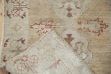 Folded corner of a distressed Oushak rug revealing the hand-knotted back and secured side cord.