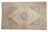 A vintage distressed Oushak carpet with a stepped sky blue medallion and spandrels on a sandy beige field.