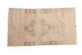 Distressed vintage Oushak rug with faded floral medallion, primitive border, dusty rose, ivory, and coffee brown.