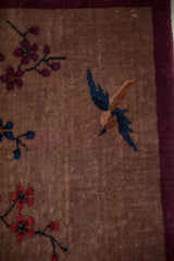 Detail of a cobalt blue bird and burgundy blossoms on the even pile of a pictorial rug.