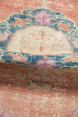 Distressed Oushak rug's rolled pile, highlighting worn texture and cantaloupe, teal, magenta tones.