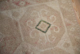 Close-up of a distressed rug's low pile, showing a green diamond motif among sand and blush tones.