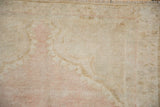 Hand-knotted texture of a distressed Oushak rug with even wear and pale pink tones.
