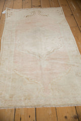 Perspective view of a distressed Oushak runner's even wear and faded pink and ivory medallion.