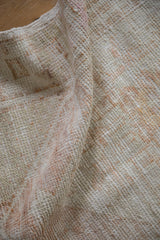 Detail of the distressed, hand-knotted texture on a vintage rug with ivory and pale rust hues.