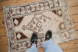 Distressed hand-knotted Oushak rug with ivory field, brown geometric motifs, and dusty blue details.
