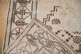 Vintage Oushak rug corner showing dark brown geometric patterns, worn ivory pile, and hand-knotted reverse.