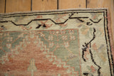 Distressed Anatolian rug corner: worn pale red, sage, ivory pile with meandering brown border.