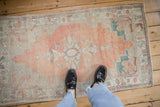A standing view of a distressed Oushak rug runner with soft cantaloupe, ivory, and mint green colors.