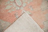 Corner of a distressed Oushak rug showing its hand-knotted ivory foundation and low pile.