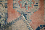 Distressed vintage Oushak rug corner showing cantaloupe and beige pile, geometric patterns, and sturdy woven back.