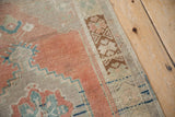 Distressed vintage Oushak rug corner showing worn cantaloupe field, blue zigzag motifs, and brown geometric border.